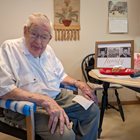 Lester Donley, DO, (COM 1952) sits at a kitchen table smiling next to a family photo. 